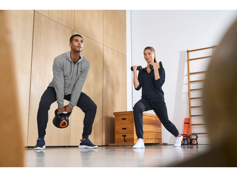 Muškarac i žena vježbaju u fitness odjeći, s girjom i bučicama u teretani.