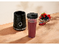 Crni osobni blender s bobičastim smoothiejem i zdjelom bobičastog voća na drvenom stolu.