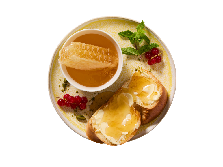Med u saću, tost s maslacem i medom, crveni ribiz i menta na tanjuru.