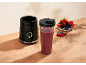 Crni osobni blender s bobičastim smoothiejem i zdjelom bobičastog voća na drvenom stolu.