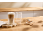 Dvije čaše za latte macchiato, jedna puna, druga prazna, s keksima na drvenom stolu.