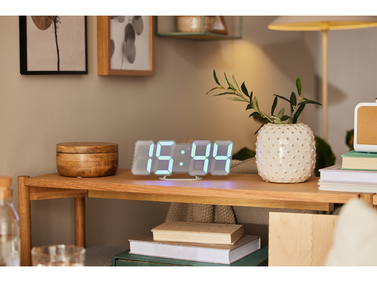 Digitalni sat prikazuje 15:44, vaza s granama i drvena kutija na noćnom ormariću.