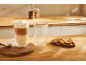 Latte macchiato u dvostrukoj čaši s biskotima na drvenoj kuhinjskoj ploči.