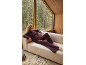 Žena u bordo pidžami opušta se na kauču pored prozora s pogledom na šumu.