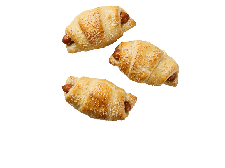 Tri slana kroasana s hrenovkom i sezamom na crnoj pozadini.