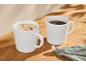 Dvije šalice kave, jedna s cappuccinom, druga s crnom kavom, na drvenom stolu.