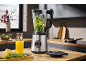 Blender sa zelenim sastojcima na kuhinjskom pultu, s sokom i povrćem pored.