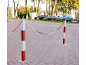 Crveno-bijeli stupići s lancima blokiraju popločano područje, automobili u pozadini.