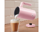 Ružičasti pjenilac mlijeka ulijeva pjenu u čašu lattea na drvenom pultu.