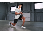 Muškarac u sivoj majici i crnim kratkim hlačama radi iskorake s bučicom.