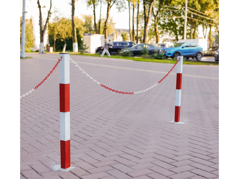 Crveno-bijeli stupići s lancima blokiraju popločano područje, automobili u pozadini.