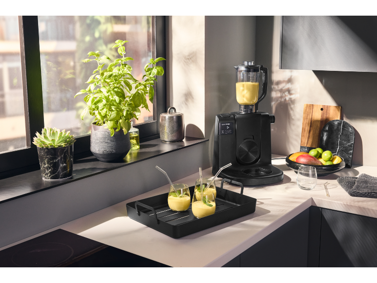 Crni kuhinjski robot s blenderom i pladnjem sa smoothiejima u modernoj kuhinji.