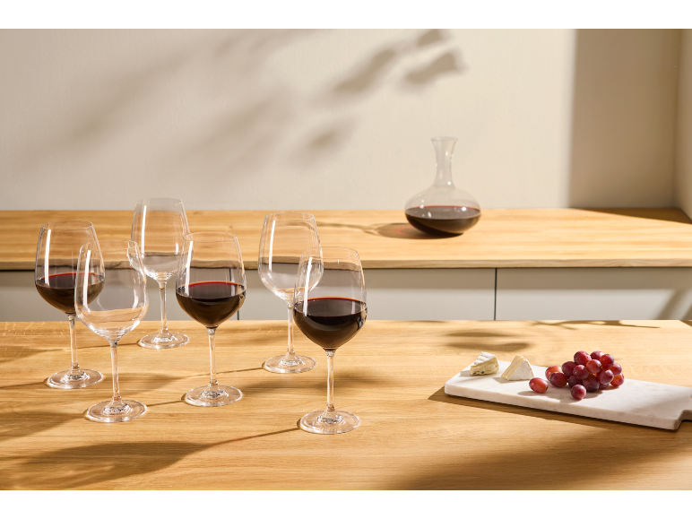 Crno vino u čašama i dekanteru na drvenom stolu sa sirom i grožđem.