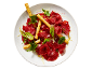 Goveđi carpaccio s rikulom, začinskim biljem i grissini štapićima na bijelom tanjuru.
