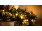 Božićni vijenac osvijetljen toplim svjetlima na svijetloj površini.
