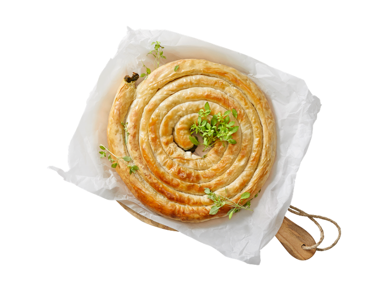 Spiralni burek sa sirom i špinatom s svježim začinskim biljem na papiru za pečenje.