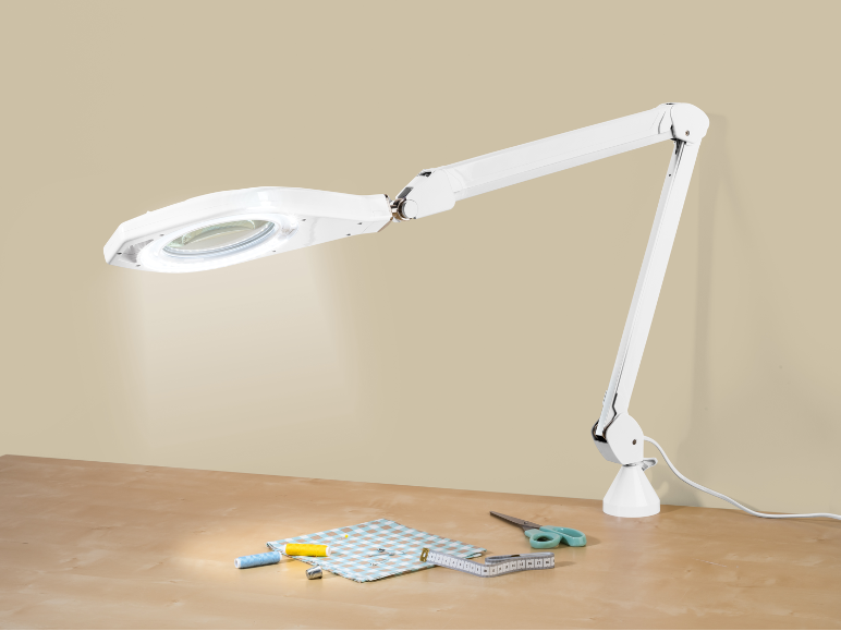 Bijela LED lupa s osvjetljenjem iznad stola s priborom za šivanje.