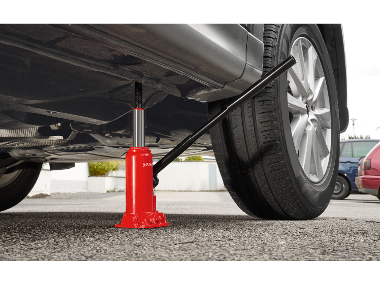 Crvena hidraulična dizalica podiže automobil za promjenu kotača.