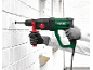 Muškarac buši rupu u bijelom zidu od opeke udarnom bušilicom.