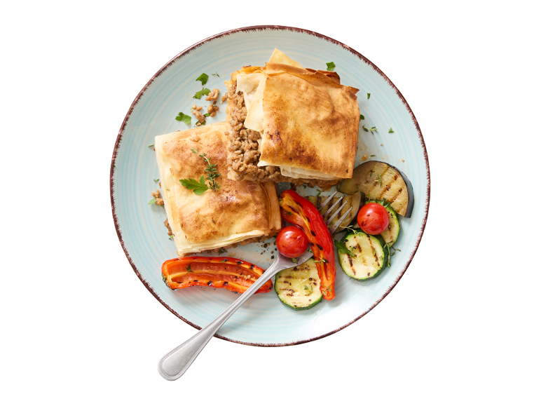 Pita od mljevenog mesa s povrćem na žaru i cherry rajčicama na plavom tanjuru.