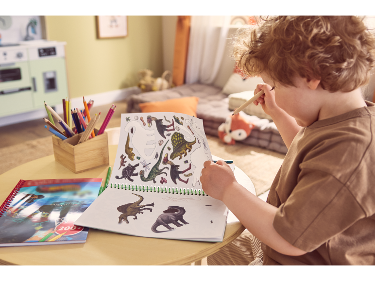 Dijete crta dinosaure u bojanci s bojicama na stolu.