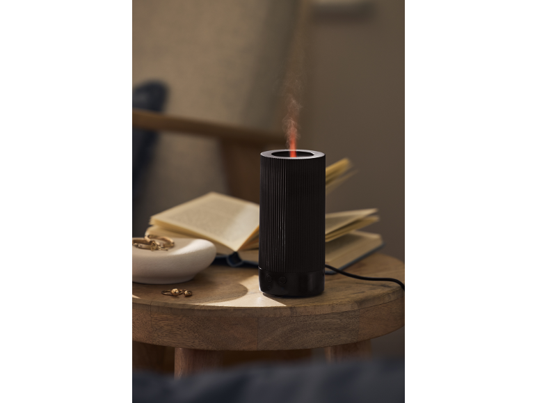 Crni aroma difuzor s parom na drvenom stolu s knjigama i nakitom.