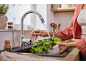 Žena pere zelenu salatu pod modernom kuhinjskom slavinom s LED svjetlom.