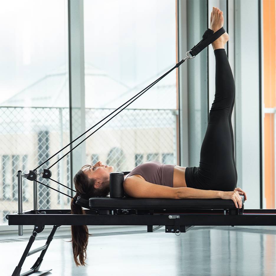 Žena radi vježbu za noge na pilates reformer spravi.