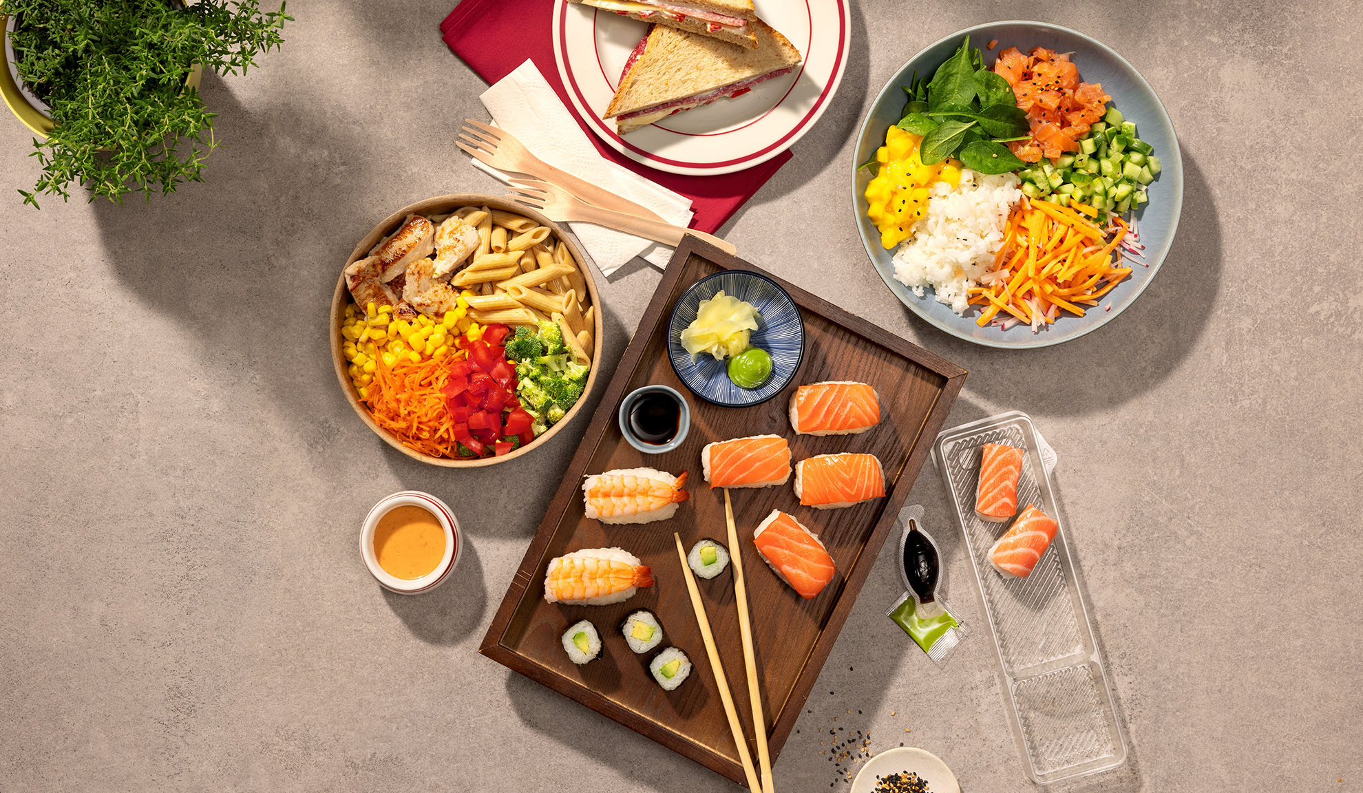 Pogled odozgo na razna jela za van: sushi, poke zdjela, salata od tjestenine i sendviči.