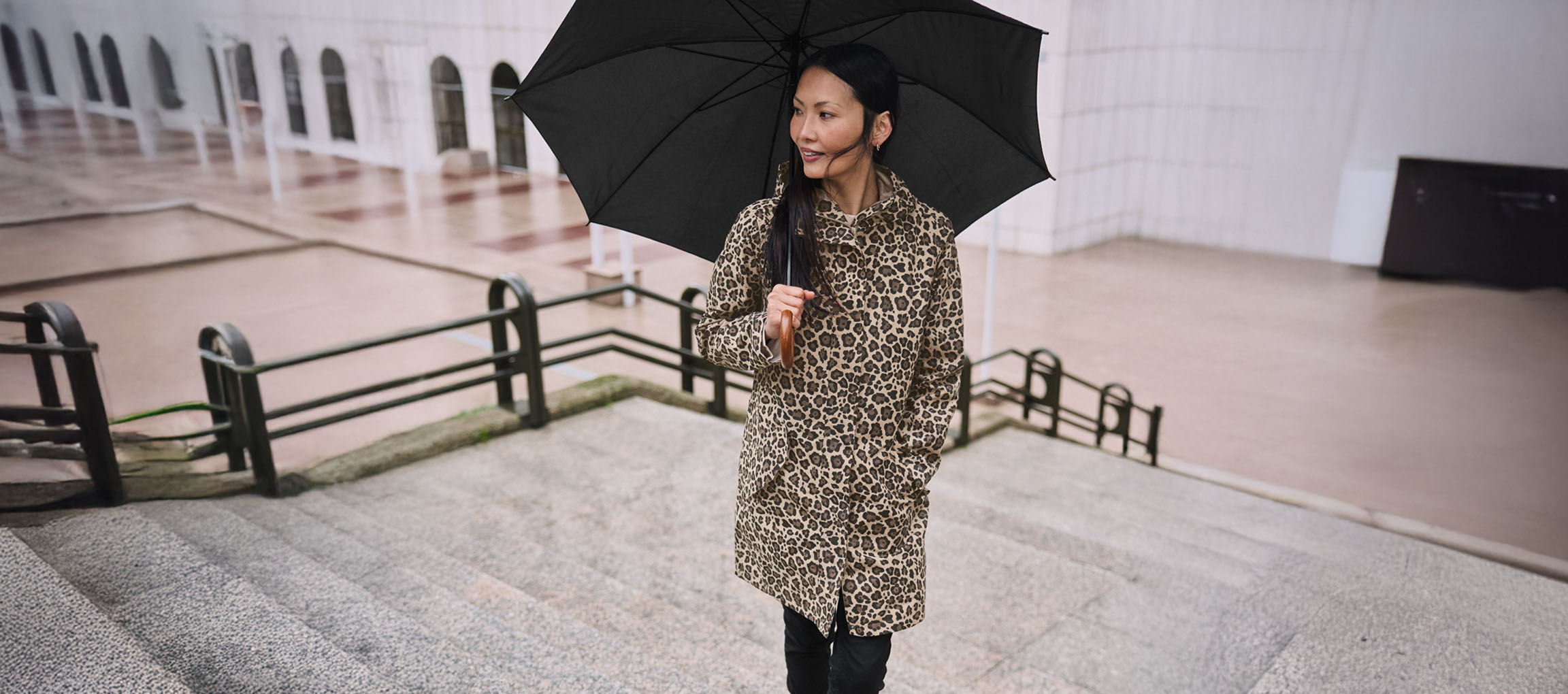 Žena u kaputu s leopard uzorkom s kišobranom na stepenicama.