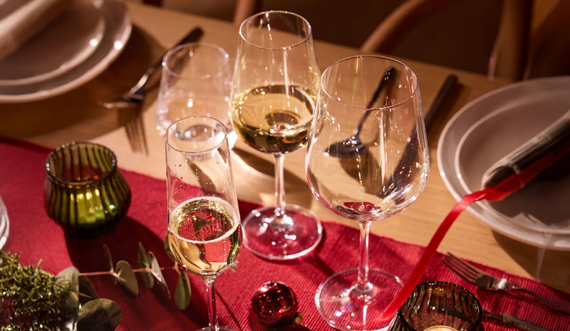 Svečano postavljen stol s čašama za vino, čašom za šampanjac i božićnim ukrasima.