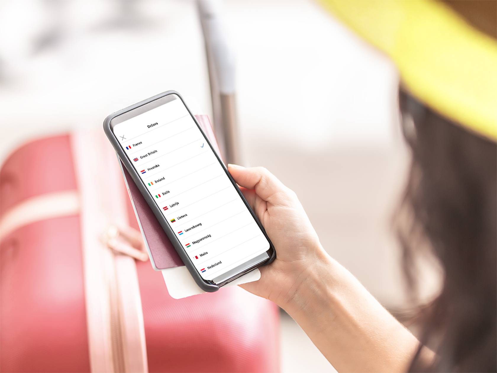 Osoba drži pametni telefon s popisom zemalja, uključujući Hrvatsku, Francusku i Veliku Britaniju.