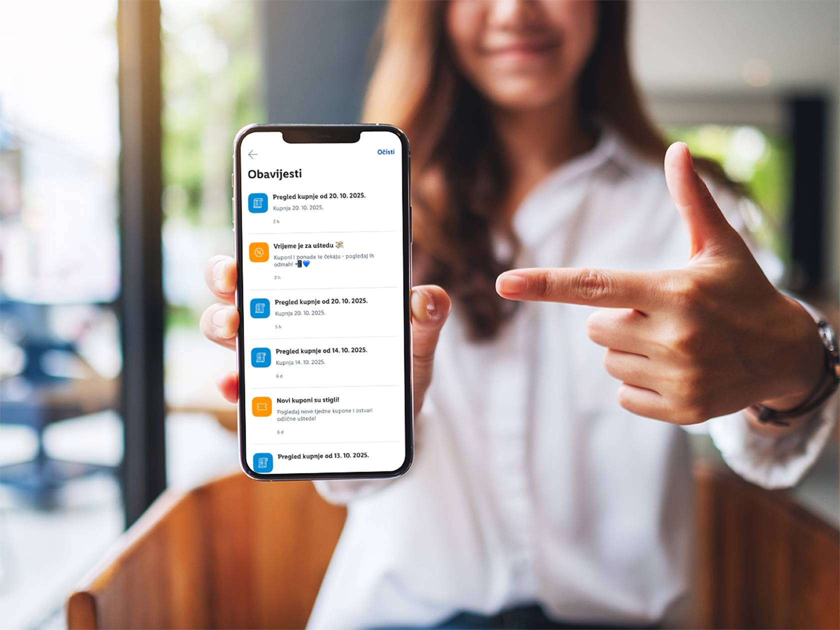 Žena drži pametni telefon s aplikacijom za obavijesti o kupnji i kuponima, pokazujući na ekran.