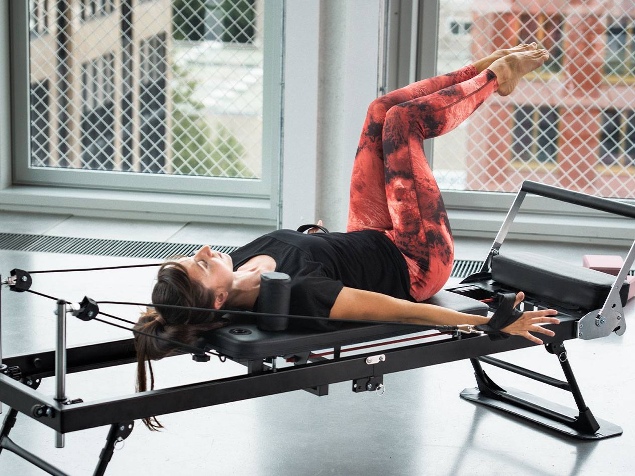 Žena vježba Pilates na reformer spravi, u crvenim i crnim tajicama