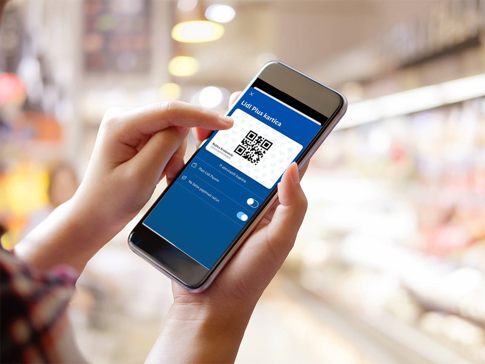 Osoba drži pametni telefon s aplikacijom Lidl Plus kartice i QR kodom u trgovini.