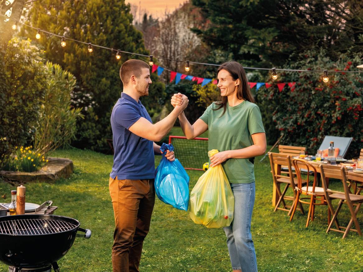 Par s vrećama za smeće u vrtu s roštiljem i vrtnim namještajem.