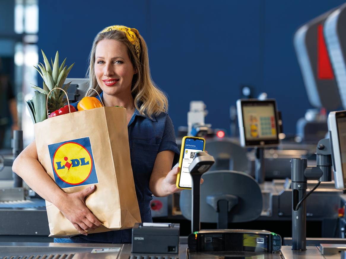Žena s vrećicom namirnica i telefonom s QR kodom na blagajni.