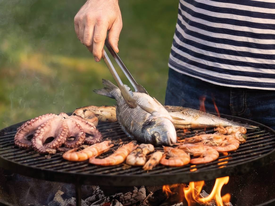 Muškarac peče ribu, hobotnicu i škampe na roštilju na otvorenom.