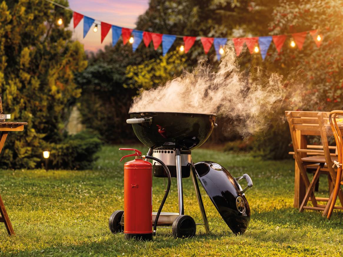 Roštilj na ugljen s dimom, vatrogasnim aparatom i zastavicama u vrtu.