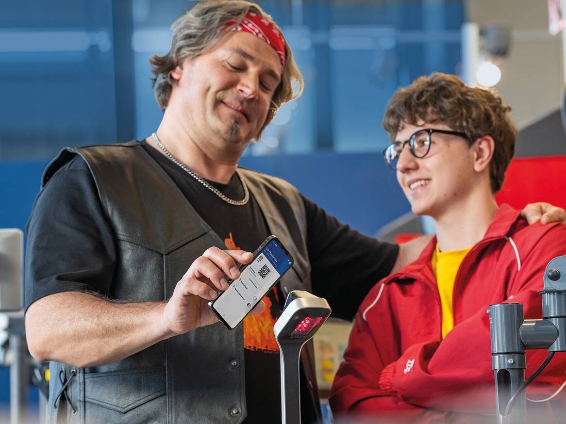 Muškarac skenira QR kod s telefona na blagajni, dok tinejdžer stoji pored njega.