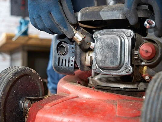 Rukavice mijenjaju svjećicu na crvenoj kosilici.