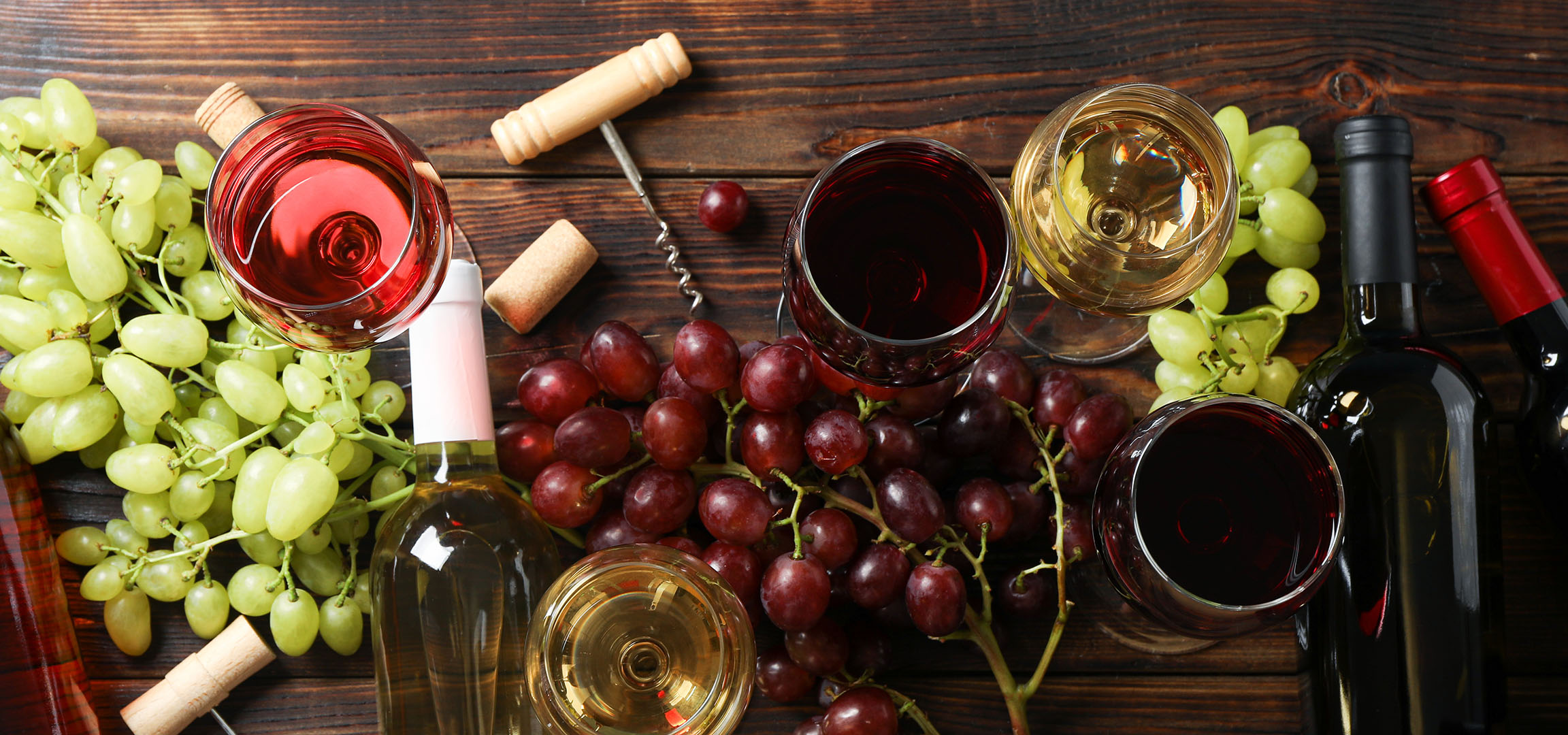 Razna vina, grožđe i pribor za vino na drvenom stolu.