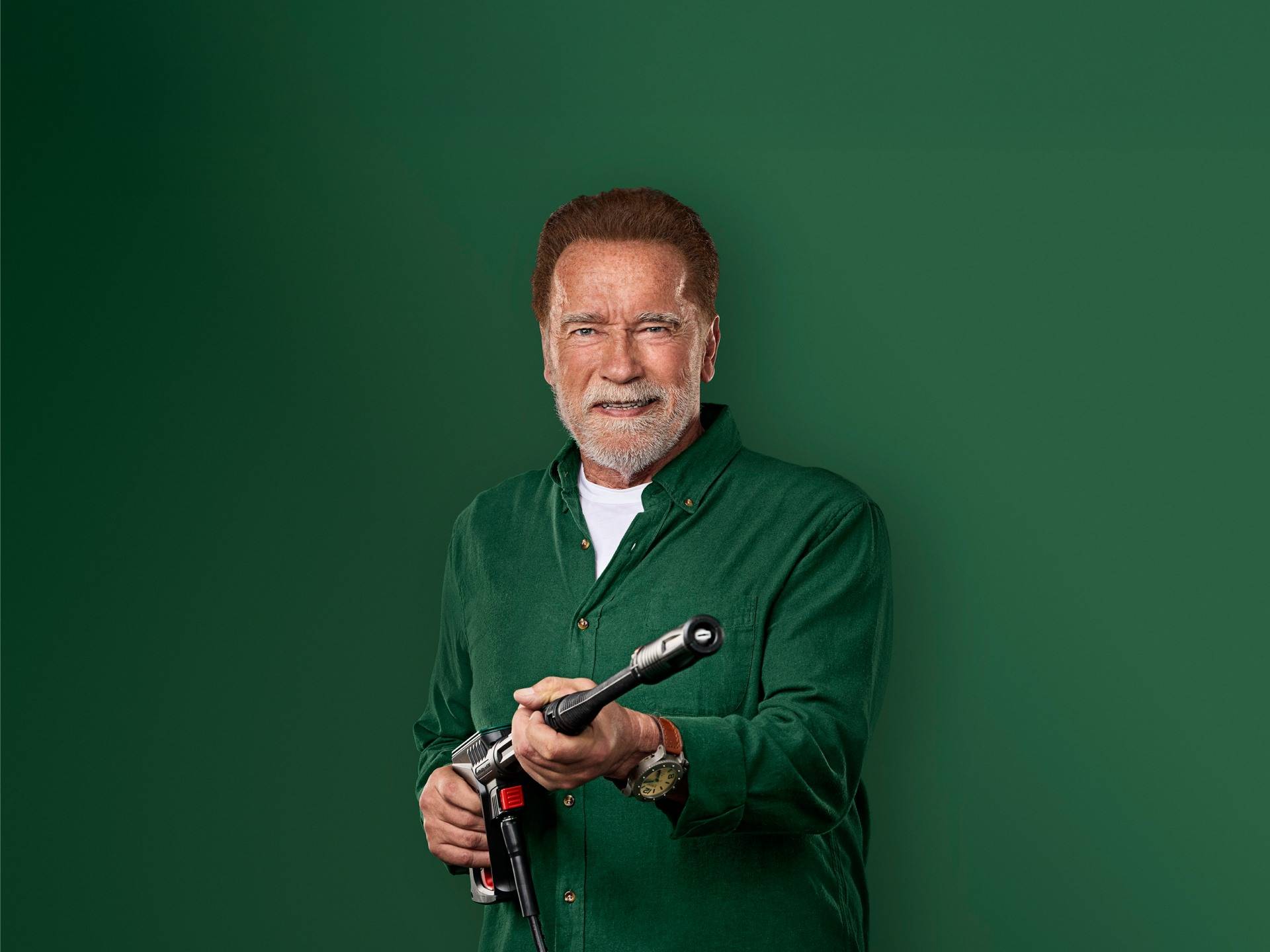 Arnold Schwarzenegger se smiješi, držeći pištolj za pranje pod pritiskom.