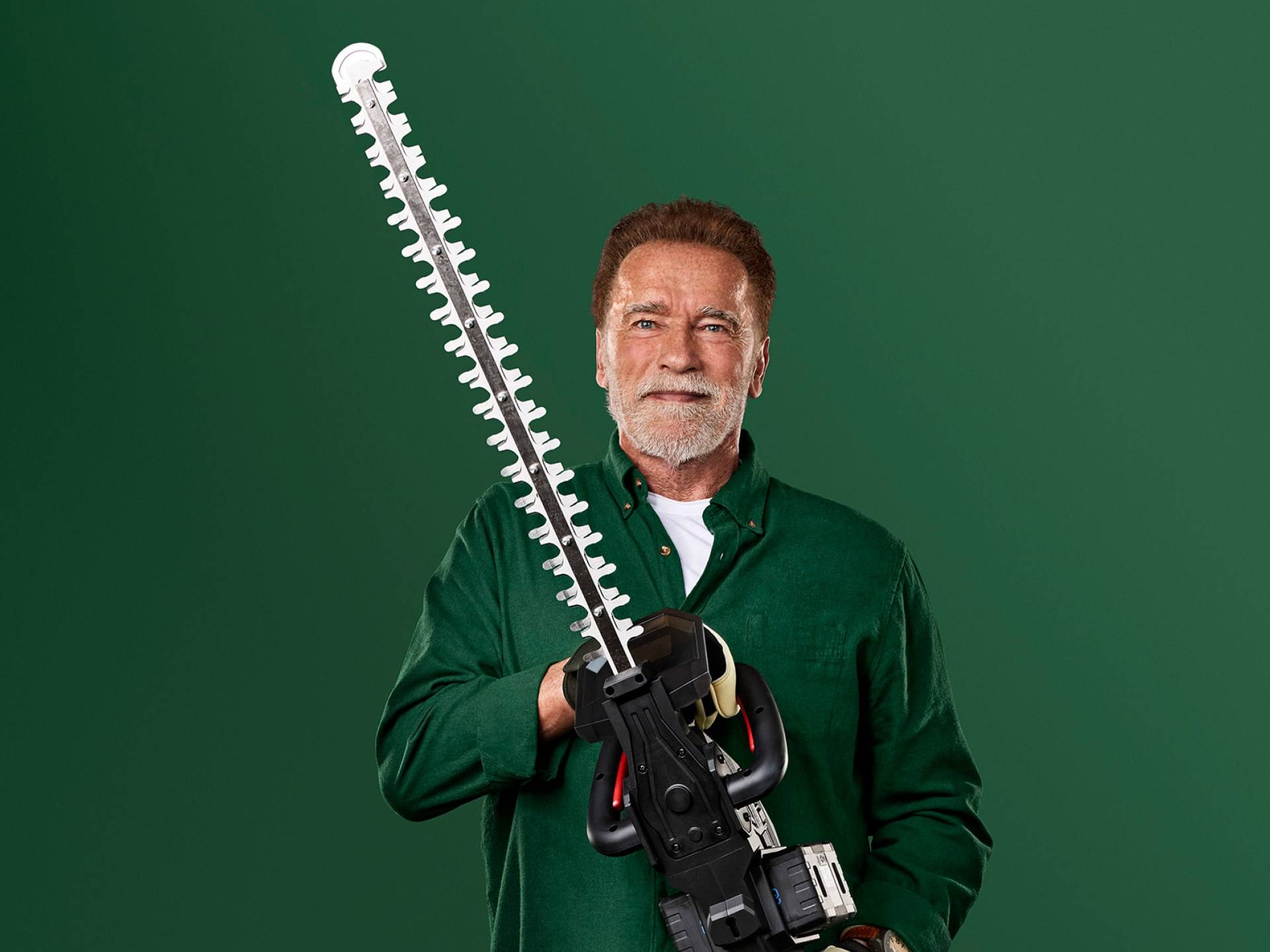 Arnold Schwarzenegger drži velike škare za živicu na zelenoj pozadini.
