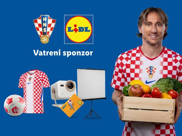 Nogometaš u kockastom dresu drži sanduk s voćem i povrćem, uz nogometnu loptu, dres, projektor i bon.