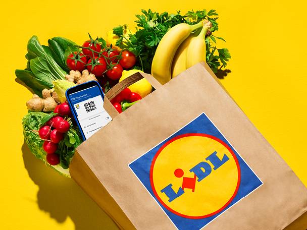 Papirnata vrećica s bananama, rajčicama, rotkvicama, đumbirom i zelenim lisnatim povrćem, uz pametni telefon s QR kodom.