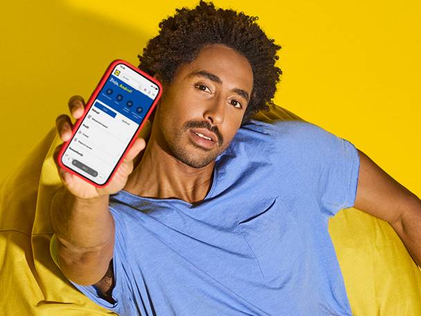 Muškarac drži pametni telefon s aplikacijom, sjedi na žutoj vreći za sjedenje.