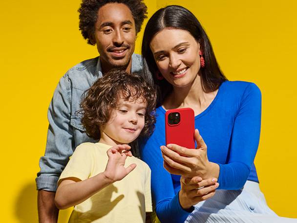 Obitelj gleda u pametni telefon s crvenom maskom, na žutoj pozadini.