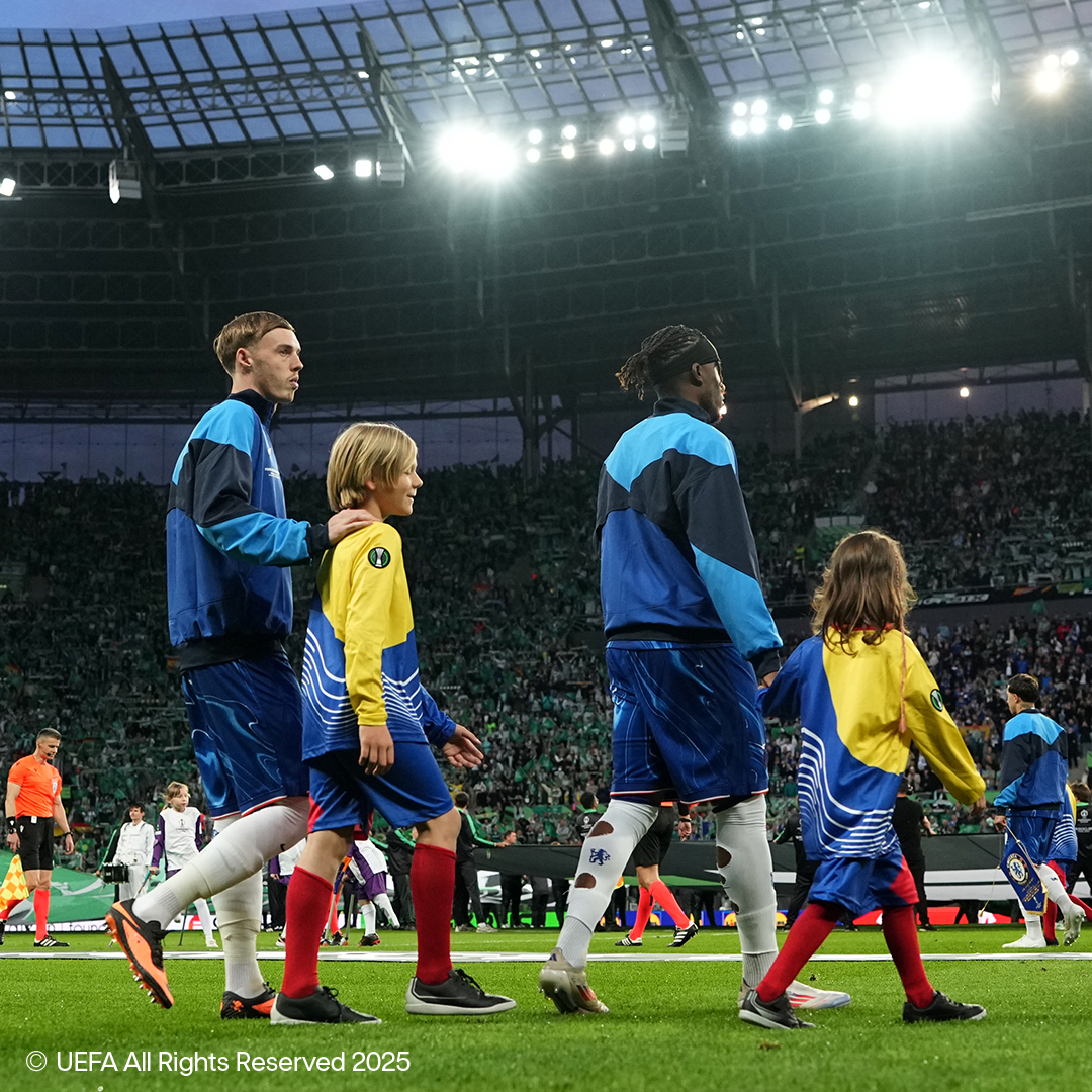 Nogometaši i djeca hodaju po terenu punog stadiona.