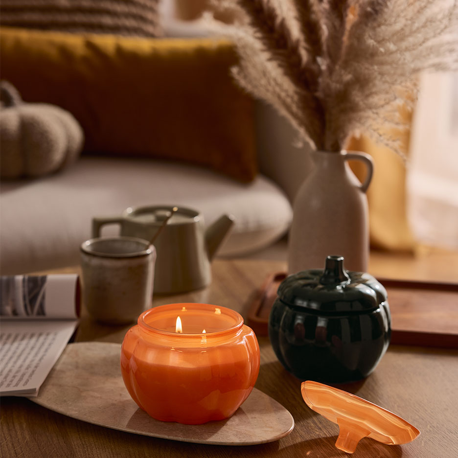 Svijeća i posuda u obliku bundeve na stoliću za kavu s jesenskim dekorom.